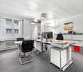 modern office with white walls, gray carpet, white desks, black chairs, computer monitors, radiator, cabinets, painting, flag