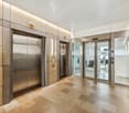 Lobby area with tiled flooring, steel elevator doors, glass doors, light fixtures, and control panels.