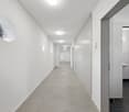 long hallway, white walls, circle window, gray tile floor, square ceiling lights, bathroom door
