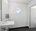 Modern, clean bathroom with white walls, tiled flooring, round window, white sink, and mirror.