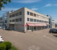 Modern office building, two-story, beige exterior, glass windows, red awnings, parking lot