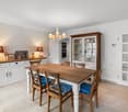 White cabinetry, wooden dining table, blue cushioned chairs, wooden floor, chandelier, cabinets with glass doors, wall mounted lamps
