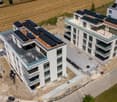 Multi-story apartment building with solar panels installed on the roof, surrounded by a grassy field and construction site