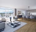 Spacious open-plan living area with large windows overlooking a balcony, hardwood flooring, modern gray furniture including a sofa, armchairs, and a glass-top coffee table, a dining table with chairs, and a fully equipped kitchen with gray cabinets.