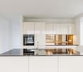 Modern kitchen with white cabinets, black granite countertops, built-in oven, double kitchen sink, stainless steel faucet