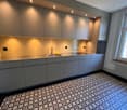 modern kitchen with gray cabinets, stainless steel countertops, tiled backsplash, under-cabinet lighting, double sink, faucet, oven, window with view