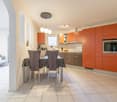 Modern kitchen, orange cabinets, dining table with four chairs, built-in oven, countertops, open area, tiled floor