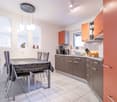 modern kitchen with island, white countertops, stainless steel appliances, open shelving, dining table and chairs, orange cabinets