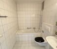 Tiled bathroom with a bathtub, shower, toilet, and vanity. The walls are covered in white tiles arranged in a grid pattern.