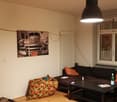 sleek lamp, modern black couch, patterned ottoman, rustic wood floor, picture of car on wall, white radiator, window with white blinds