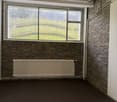 Empty room, three windows, radiator, brick walls, wooden flooring