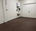 empty room with white brick walls, brown carpeted floor, sink, and pipes on the wall