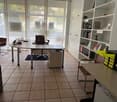 Office room: desks, chairs, bookshelves, a table with a vase of flowers, large windows, a glass wall, beige tiled floor