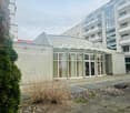 A modern building with gray concrete walls, glass doors and windows, and a small garden in front. The building is labeled as Christian Science. A tall building is on the right side. A bike is parked on the right.