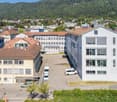 The image shows a view of a town or city, with a mix of residential and commercial buildings. The buildings have a variety of architectural styles, including some with red tile roofs and others with more modern designs. There are several multi-story build