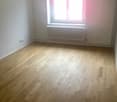 white walls, wooden floor, a window with white frames, white radiator, two white electrical outlets