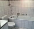 Bathroom with bathtub, toilet, sink, shower head, tiled walls, white tiles