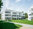 Modern apartment building with multiple balconies, well-maintained green lawn, and a pathway leading to the entrance.
