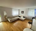 L-shaped sofa, TV, mirror, wooden floor, white walls, white curtains, glass door to balcony