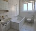 Bathroom with white tiles, bathtub, sink, toilet, shower head, window