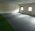 Empty room with green carpet, concrete flooring, windows, heaters, and a whiteboard mounted on the wall.