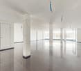 large room with white walls, grey tiles, 4 white pillars, large open windows, and glass doors