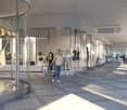 The image shows a modern shopping mall interior with glass storefronts, a long hallway with tiled flooring, and people walking through the space. There appears to be a balcony or terrace visible in the background.