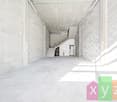 Long, narrow hallway with concrete walls and floors, stairs leading up, and a small room or space visible at the end of the hallway