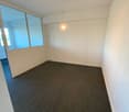 Empty room with grey carpet, white walls, ceiling lights, glass doors, and windows.