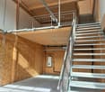 wooden floor, walls made of wood panels, balcony, stairs to balcony, metal railing, pipes and cables attached to the ceiling