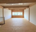 an empty room with wooden floors and a ceiling with visible beams, with a staircase on the left