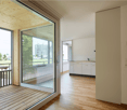 wooden floor, large glass doors, balcony, white kitchen cabinets, white walls