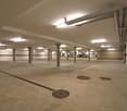 empty underground parking lot with several concrete pillars and lights mounted on the ceiling