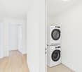 Utility room, white walls, wooden floor, white washer and dryer stacked