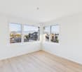 Empty room, white walls, wooden floor, large windows with mountain views