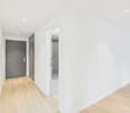 Empty hallway, with white walls, wooden floor, grey doors, and a shower room