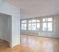 Wooden floors, white walls, multiple large windows, and no furniture