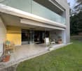 Modern house with glass walls, yellow exterior, large terrace, wooden furniture, potted plants, green lawn
