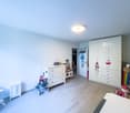 A room with white walls, wooden floor, white cabinets, a white piano, a stroller, and a white stool.