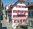 white painted house, red shutters, balcony with red chairs, fountain at front