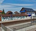Train station with graffiti on the wall, solar panels on the roof, houses in the background, and a platform with a shelter