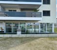 Modern building with glass walls, balcony, and a small garden in front