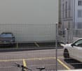 fenced parking area with 4 parking spots, 2 parked cars and a bicycle in front of a building
