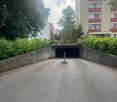 an empty parking lot beneath an overpass with gray concrete barriers and surrounded by greenery