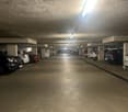 Well lit parking lot with multiple parked cars, concrete floor, pillars, and lights