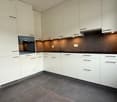 Modern kitchen with white cabinets, black countertops, and gray tiled floor. Equipped with an oven, sink, and faucet.
