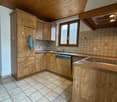 A kitchen with wooden cabinets, tiled floor, and a sink with a faucet. There is a dishwasher under the countertop, and a towel is hanging on a cabinet door. The window provides natural light, and the ceiling has a light fixture.