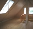 Empty attic room with wooden floors, two windows, and a wooden staircase.