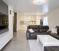 modern living room, black leather sofa, white coffee table, large flat screen TV, white cabinets, white radiator, wooden floor