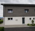 modern house, gray and white exterior, large windows, entrance with glass door, paved driveway, small garden
